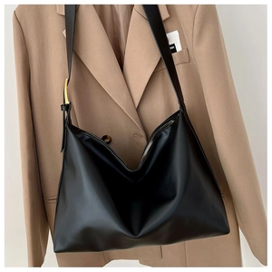 Detail of a black matte leather hobo bag with gold hardware and wide strap on office wear