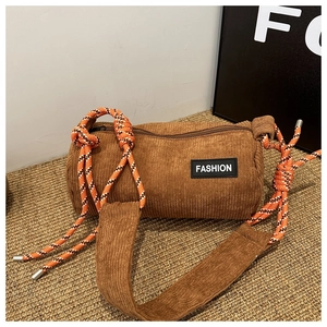 Detail of a brown corduroy cylinder crossbody bag with fashion tag and woven rope knots