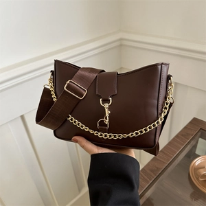 Deep brown leather bucket bag with gold chain and woven shoulder strap on minimalist backdrop