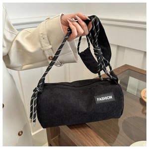 Detail of a black corduroy cylinder bag featuring a woven rope strap and FASHION patch