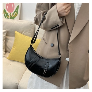 Detail of glossy black crescent shoulder bag with silver hardware on a beige suit