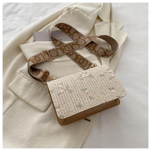 Detail of straw woven crossbody bag with floral embroidery and patterned wide strap