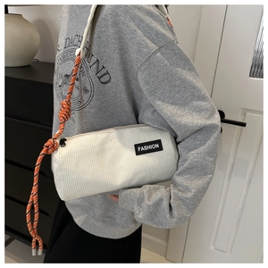 Detail of corduroy crossbody bag with fashion label and orange rope strap showing texture