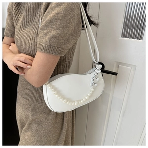 Close-up of white hobo bag with pearl chain and silver heart charm on model shoulder