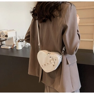 Close-up of beige heart-shaped crossbody bag with metal rivets and zipper detail