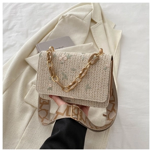 Detail of floral embroidery on beige straw bag with textured strap and chain handle