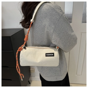 Detail of corduroy cylinder bag with orange woven rope strap and fashion label