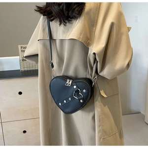 Detail of a black heart-shaped crossbody bag with silver hardware on a beige trench coat