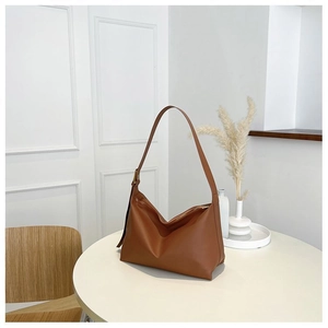 Close-up of caramel leather hobo bag with gold hardware on a minimalist white table
