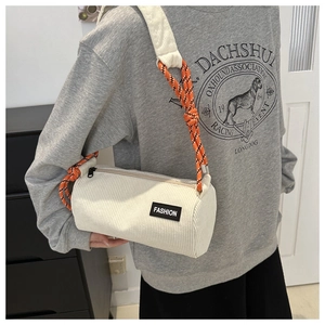 Detail of cream corduroy cylinder bag featuring colorful braided strap and fashion tag