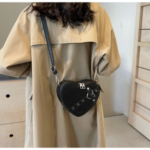 Detail of black heart-shaped crossbody bag with silver rivets worn over a trench coat