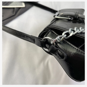 Close-up of black pleated leather handbag with silver chain and metal buckle details
