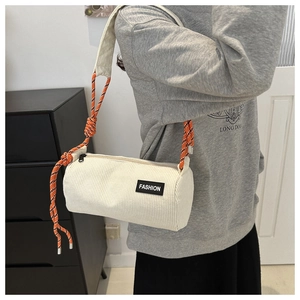 Detail of white corduroy cylinder bag featuring fashion patch and orange woven rope strap