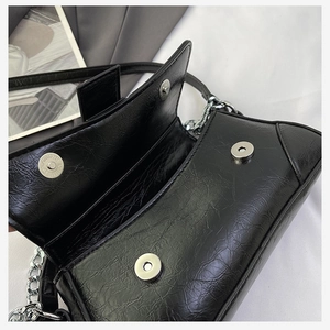 Close-up of black glossy crinkled leather bag with silver chain and magnetic buckles