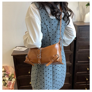 Gros plan d'un sac bandoulière en cuir marron avec boucle et anneaux métalliques sur un modèle