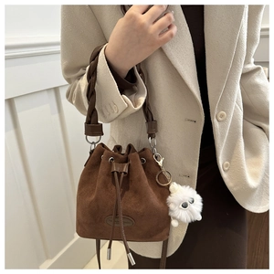 Brown faux suede bucket bag with drawstring closure and fuzzy charm on woven handle