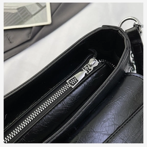 Detail view of black crocodile pattern shoulder bag with silver zippers and compartments