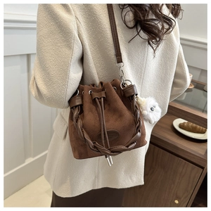 Detail of coffee brown suede bucket bag with woven handle and plush white charm