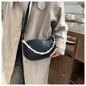 Detail of black crescent shoulder bag with pearl chain and silver heart charms in a cafe