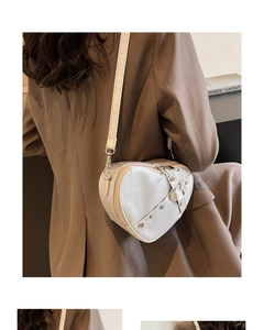 Detail of white heart-shaped crossbody bag with silver rivets worn by a model