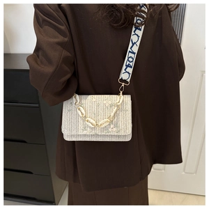 Detailed view of woven straw bag featuring floral embroidery and white chain handle