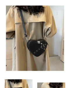 Detail of a black heart-shaped leather crossbody bag with silver zippers on a trench coat