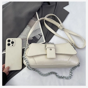 Detail of cream leather shoulder bag featuring silver chain and buckle on minimalist background