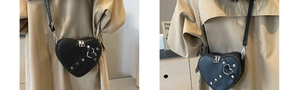 Detail of heart-shaped crossbody bag with silver studs and metal buckle on beige coat