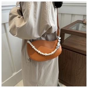 Close-up of caramel crescent bag featuring pearl chain strap and silver heart pendant detail