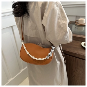 Detail of orange moon bag featuring large pearls and silver heart-shaped charms