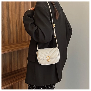 Détail d'un sac à bandoulière crème matelassé en V avec chaîne dorée sur un blazer