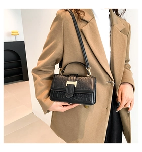 Detail of a black crocodile-embossed square handbag with a gold H-shaped metal buckle