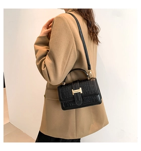 Detail of black crocodile embossed shoulder bag with golden H metal buckle on model