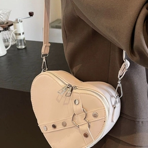 Chic beige heart-shaped crossbody bag with stud details shown on model in cafe setting