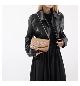 Close-up of light brown quilted leather bag with chain strap on a model wearing black jacket