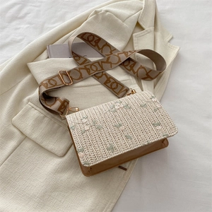 Straw crossbody bag with floral embroidery and wide woven strap on beige blazer