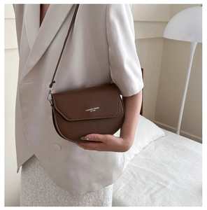 Détail du sac besace en cuir marron foncé avec rabat asymétrique et lettrage de mode