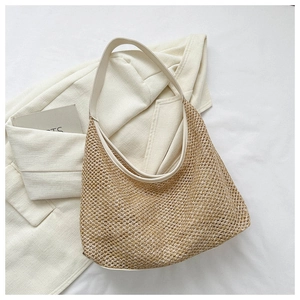Detail of the woven straw tote bag texture and wide strap on a clean white blazer