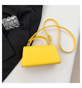 Detail shot of a bright yellow square crossbody bag with gold hardware on a white surface