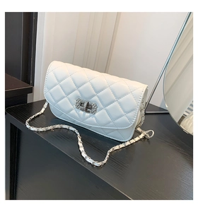 Detailed view of white quilted chain bag with crystal-encrusted turn-lock on black desk