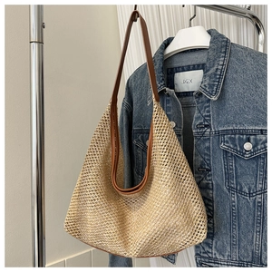 Detail view of large straw tote bag with brown leather straps on denim background