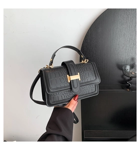 Close-up of black crocodile embossed leather handbag with gold H-shaped clasp