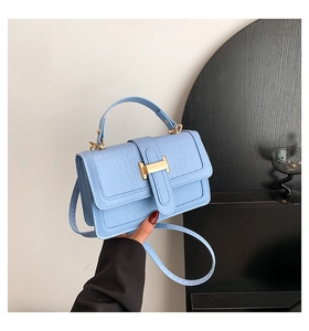 Detail of light blue faux crocodile leather bag featuring a gold H-shaped metal clasp