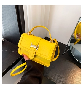Detail of yellow crocodile embossed handbag with golden buckle and sleek leather texture