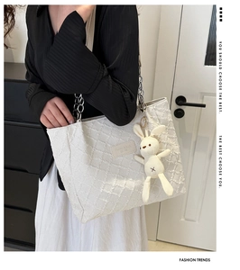 Gros plan d'un sac cabas blanc texturé avec chaîne en métal et pendentif en peluche