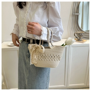 Nahaufnahme der cremefarbenen Webhandtasche mit großer Spitzenschleife und Tulpe