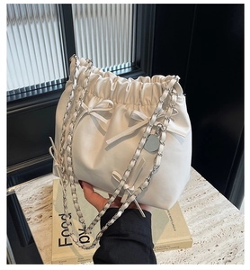 Detail of white bucket bag with bow accents and silver chain shoulder strap