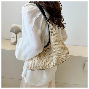 Straw hobo bag with black leather trim shown on shoulder in a minimalist indoor setting