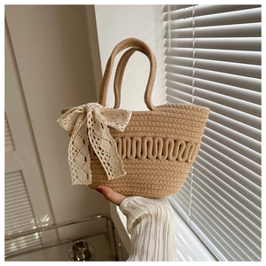 Detail einer handgewebten Strohhandtasche mit cremefarbener Spitzenschleife im Sonnenlicht