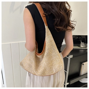 Close-up of a woven straw shoulder bag with brown leather trim on a model's shoulder